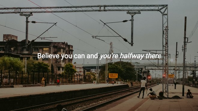 people wait quietly on a train platform at dusk under steel beams